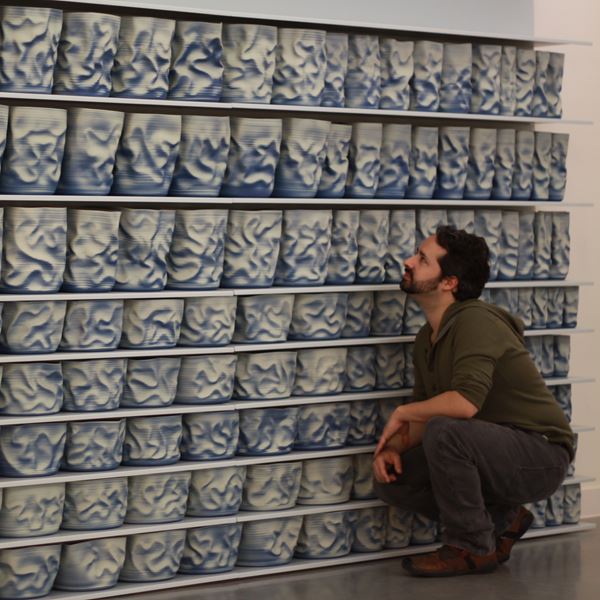 shelves of blue and cream scrunched and wrinkled looking hand thrown ceramic vessels creating a large wall mounted sculptural installation