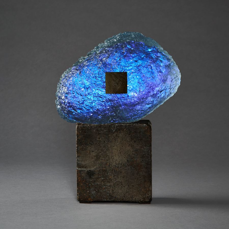 blue and dark brown meteoric hand formed glass amorphic sculpture on a weather cube base made steel