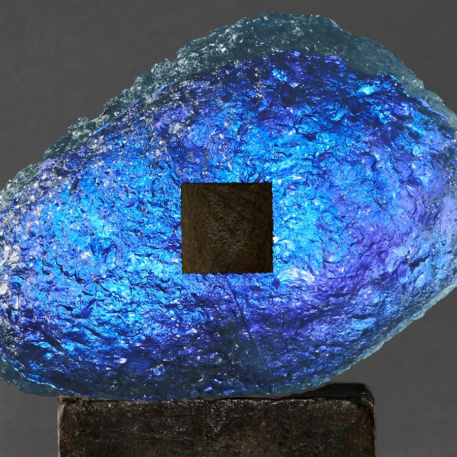 blue and dark brown meteoric hand formed glass amorphic sculpture on a weather cube base made steel