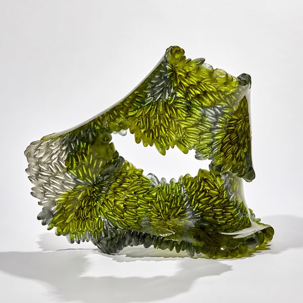 green and grey flowing squashed ring shaped textured sculpture made from cast glass