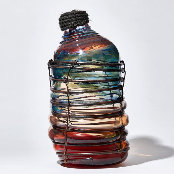 red blue and brown metal caged leaning bottle shaped glass sculpture with rope stopper detail