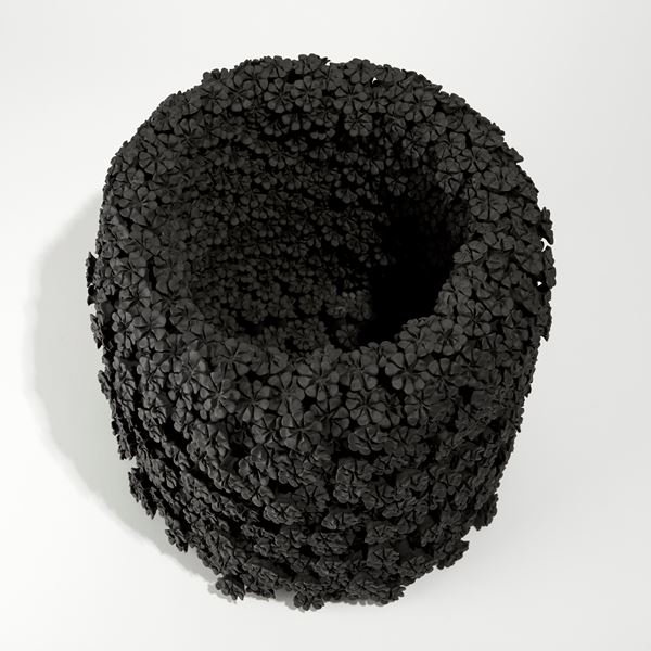 black cylinder shaped vase covered in hand made daisy shaped flowers created from clay