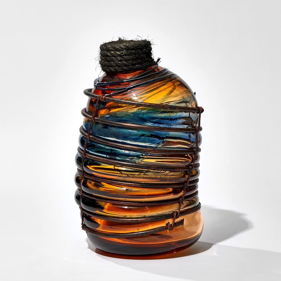 dark amber and blue aged rum bottle in copper caging with rope stopper hand made from glass