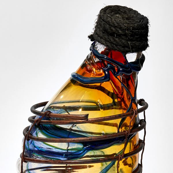 red amber and blue lopsided long necked bottle blown in to a copper cage with rope stopper hand made from glass