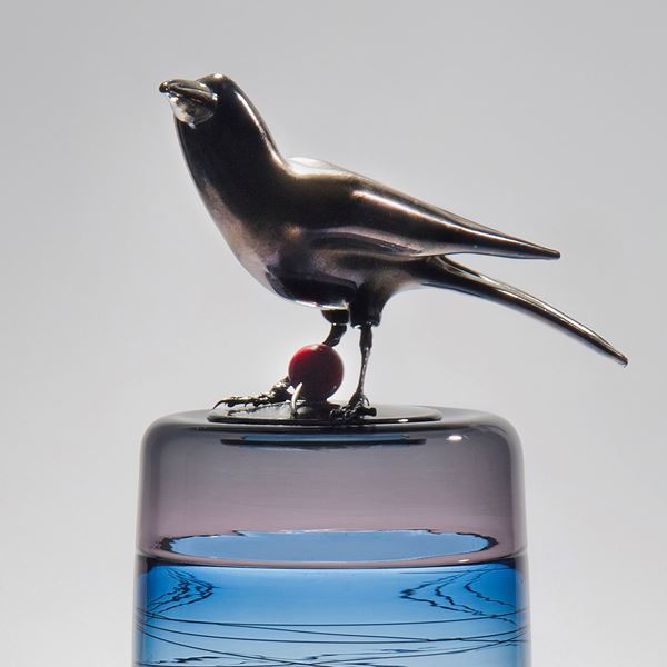 sculpted glass case in white, light blue and pink with helter skelter line pattern on exterior and stainless steel crow on top with red cherry