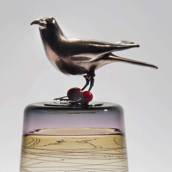sculpted clear glass vase with angled lines circling exterior with stainless steel crow sitting atop with cherries at its feet