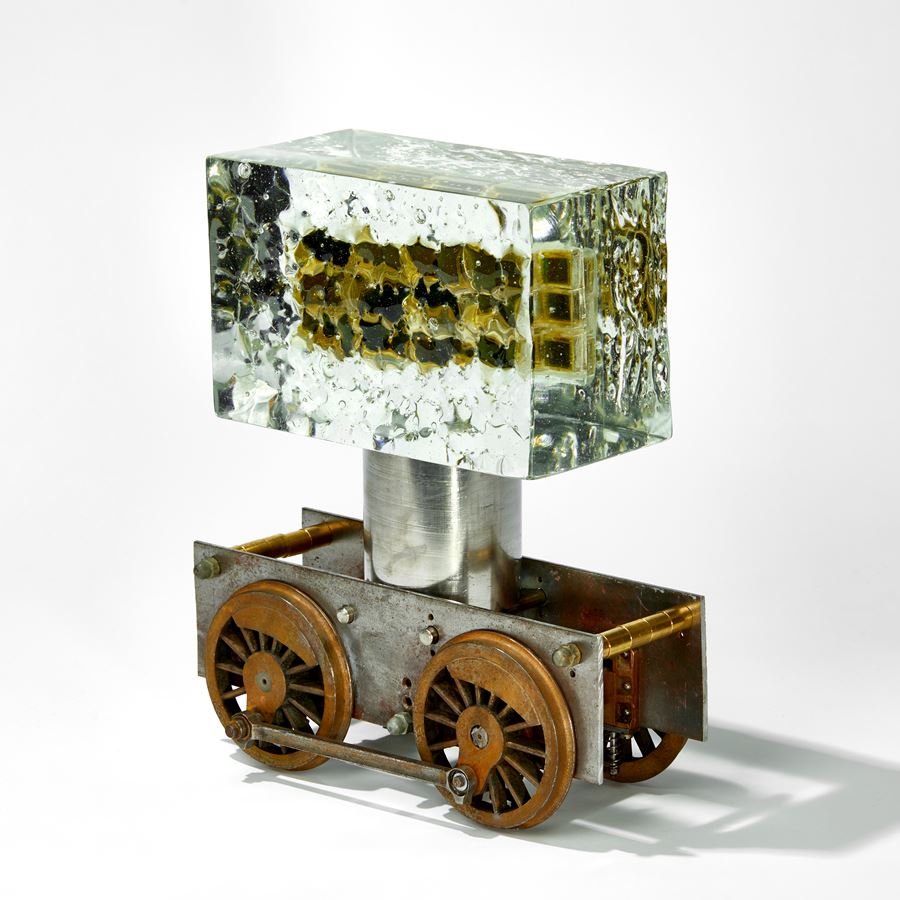 chunky ages metal train chassis with solid rectangular mass of glass above with inner winking eyes handmade from glass 