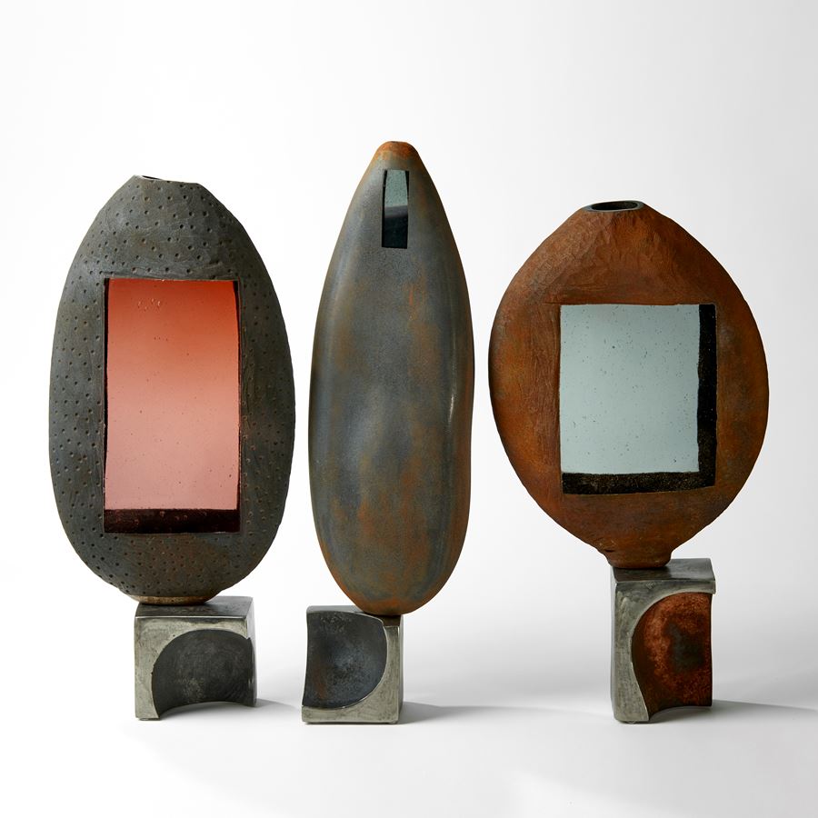 grey and rust tall ovoid sculpture with small window apertures and steel base handblown from glass