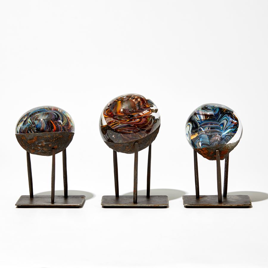 marble like round glass sculpture in clear blue and rust brown on three pronged steel base