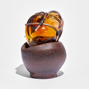 rounded red brown ceramic with cracked texture holding an amber mass of glass bound in copper pipe