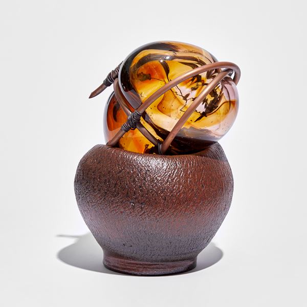 rounded red brown ceramic with cracked texture holding an amber mass of glass bound in copper pipe