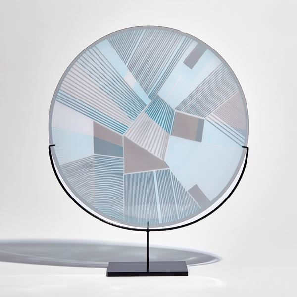 round glass plate with etched graphic pattern on the surface in soft blue and grey on a black metal stand