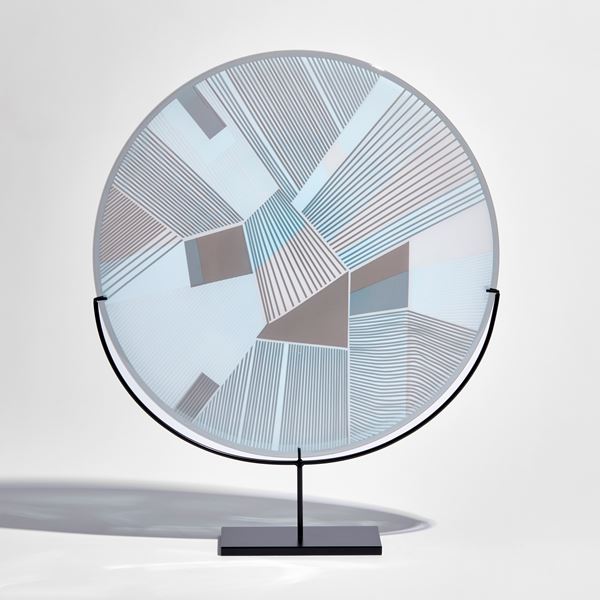 round glass plate with etched graphic pattern on the surface in soft blue and grey on a black metal stand