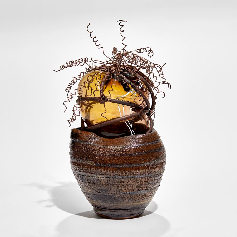 brown ridged ceramic urn containing a bursting forth bubble of amber glass bound in copper with copper wire cork screw hair