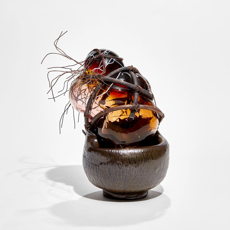 brown ceramic bowl base with copper cage holding a bursting bubble of rich amber and clear coloured glass with copper wire hair