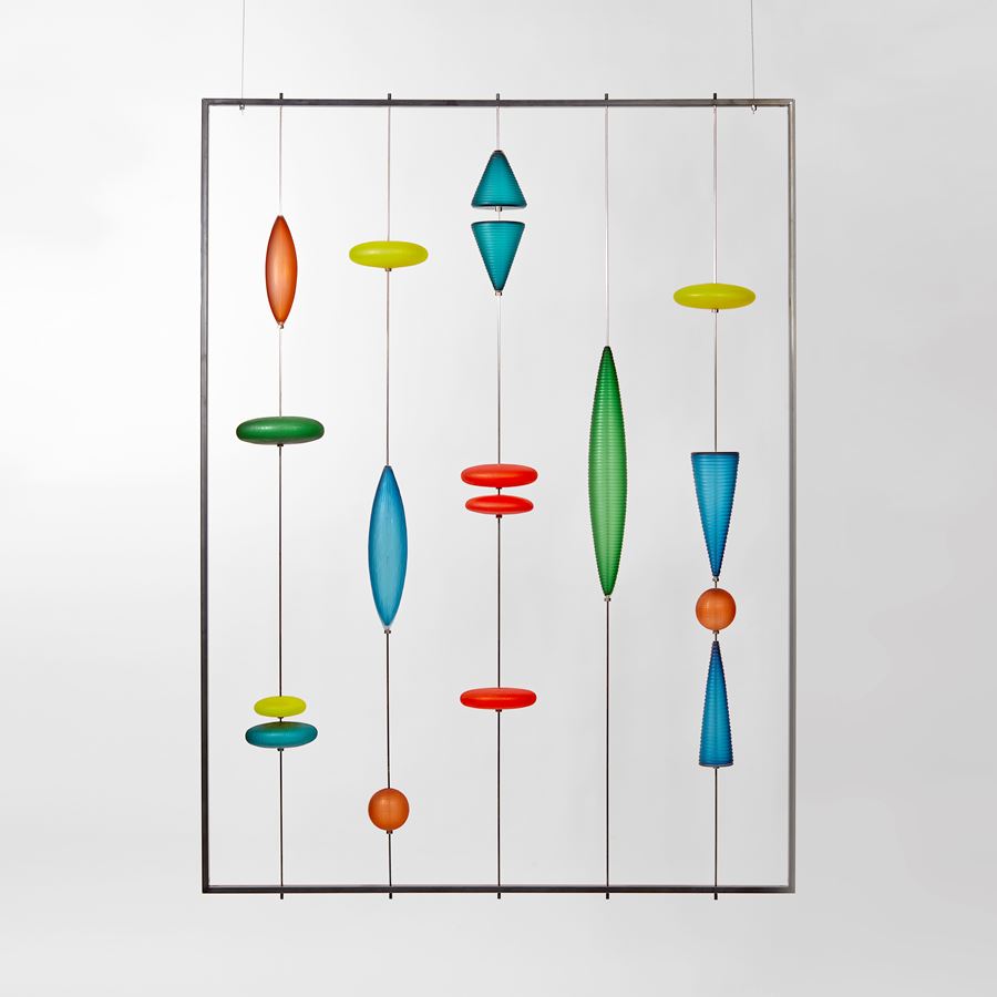 yellow red green and blue geometric shapes handmade from glass suspended in a graphic pattern within a steel frame