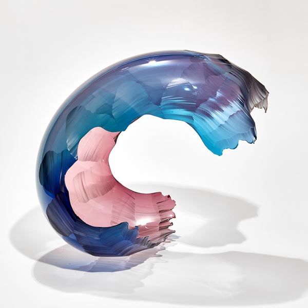 curved blue blurred to pink coloured abstract sculptural form with the appearance of a crashed wave hand made from blown glass