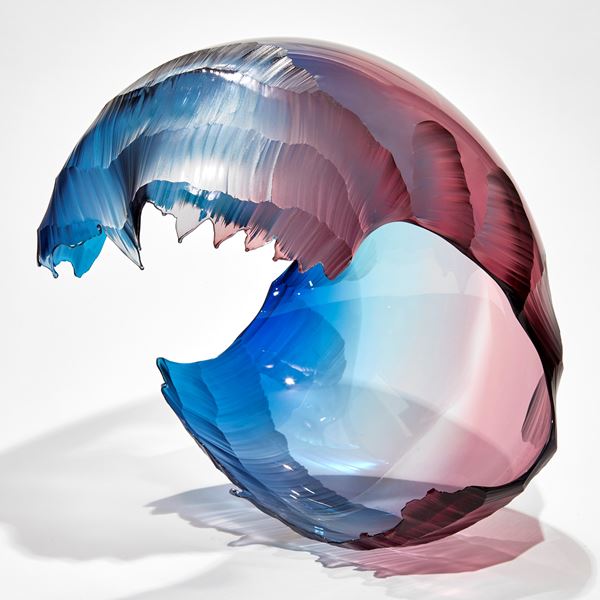 curved blue blurred to pink coloured abstract sculptural form with the appearance of a crashed wave hand made from blown glass