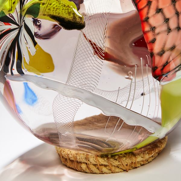 rounded vessel in clear and aubergine with latticed patches in yellow coral orange red and white hand made from glass with an ocean plastic toothbrush perched on top