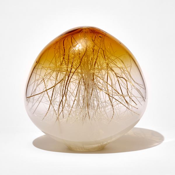 rounded sculpture with slightly pointed top fading from white clear and amber top containing thin canes in white and gold hand made from glass 
