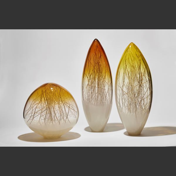 rounded sculpture with slightly pointed top fading from white clear and amber top containing thin canes in white and gold hand made from glass 