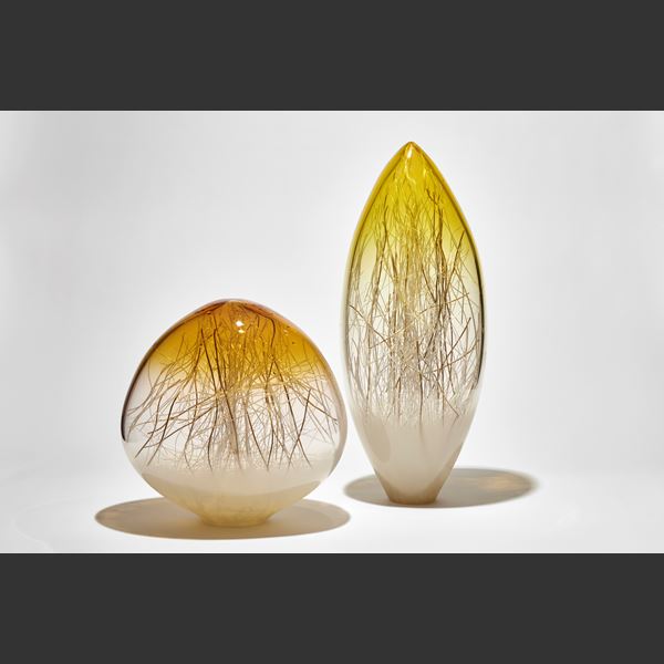 oval pointed sculpture with white base yellow top and clear middle containing thin strands in white and gold hand made from glass
