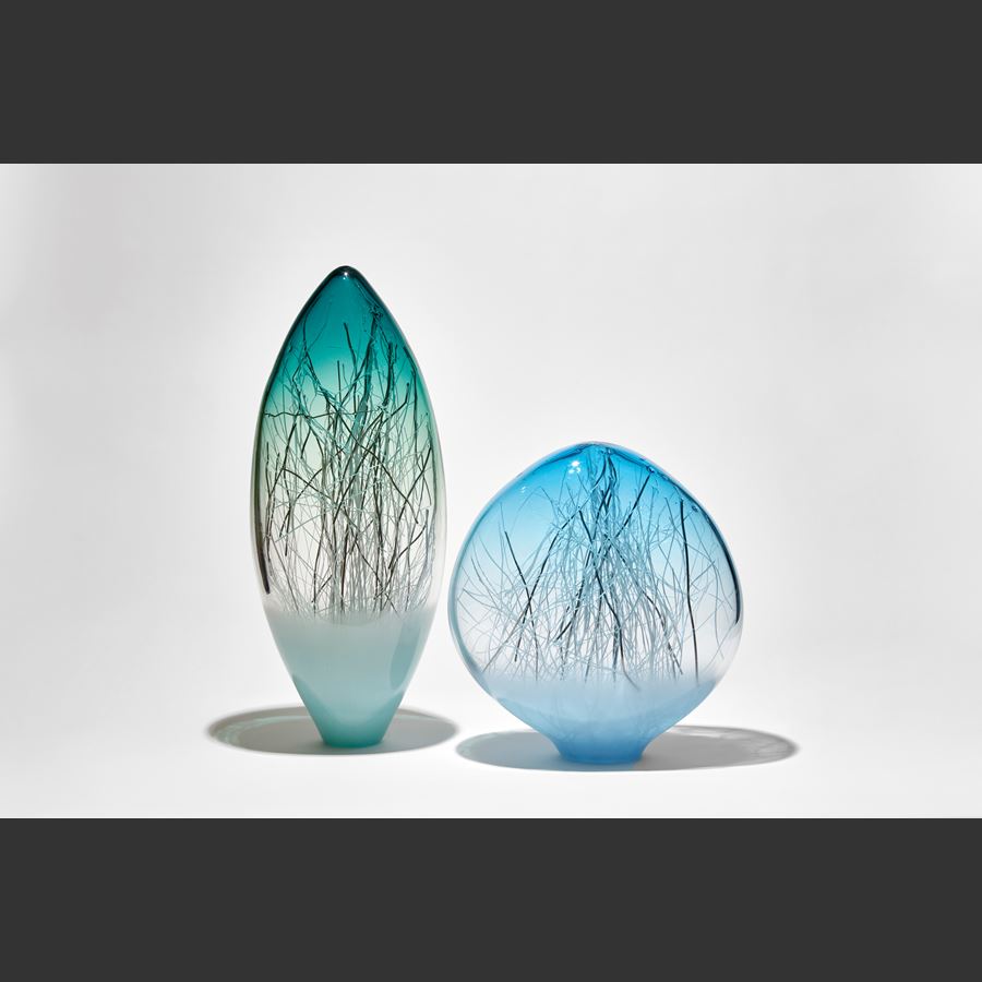 low ovoid hand made glass sculpture with soft blue base fading to clear to a bright aqua top with thin canes in white and platinum trapped inside