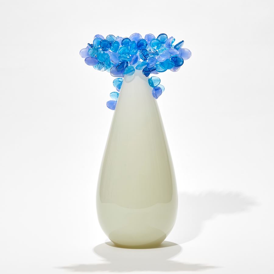 tree with teardrop shaped trunk in off white alabaster with a cluster of perched rounded leaves in soft blues and light lilac hand made from glass