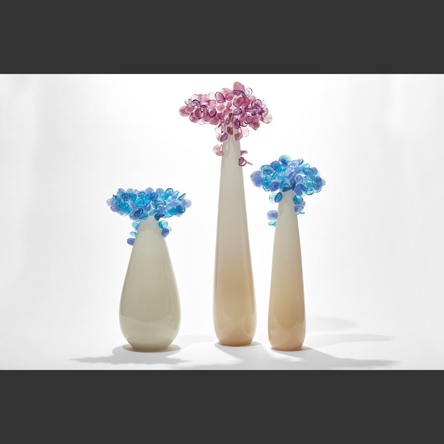 tree with teardrop shaped trunk in off white alabaster with a cluster of perched rounded leaves in soft blues and light lilac hand made from glass