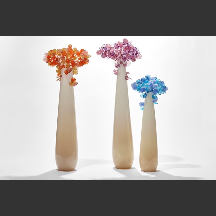tall and thin simplified tree sculpture with smooth beige and cream trunk with candy pop rounded lollipop leaves clustered at the top hand made from glass