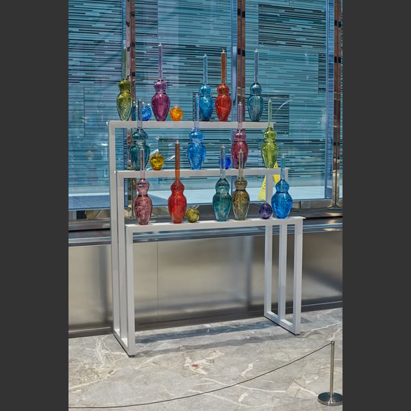 tall white three tiered metal frame with perched large scientific looking bottles each in its own colour handmade from glass