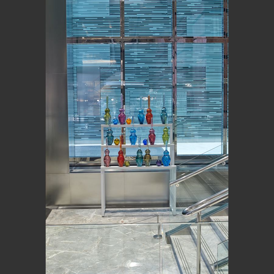 tall white three tiered metal frame with perched large scientific looking bottles each in its own colour handmade from glass