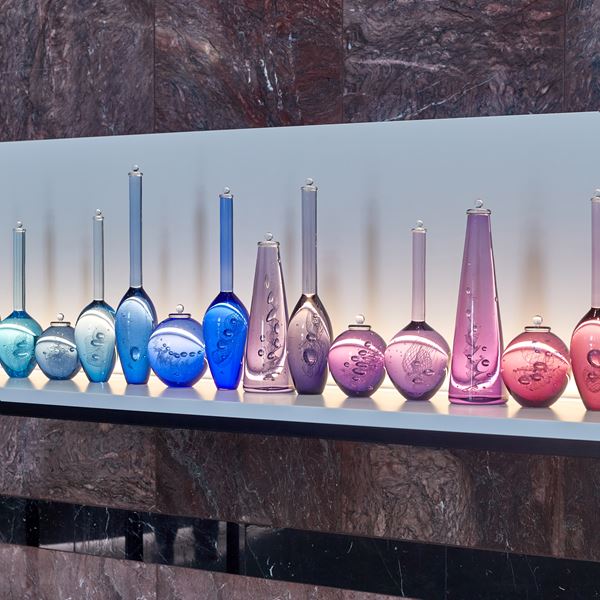 sixteen scientific looking solid bottles all different shapes each a different colour moving from aquas blues to pinks and rubies each hand made from glass