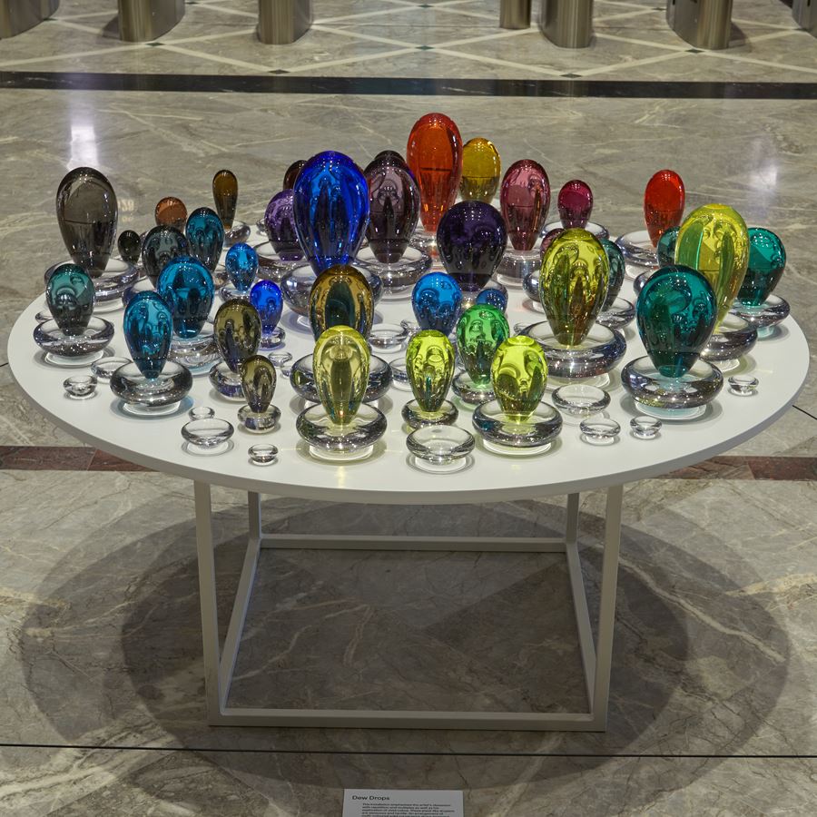 an installation consisting of a multitude of coloured droplets with a clear base each one a different colour creating a rainbow of hues handmade from glass