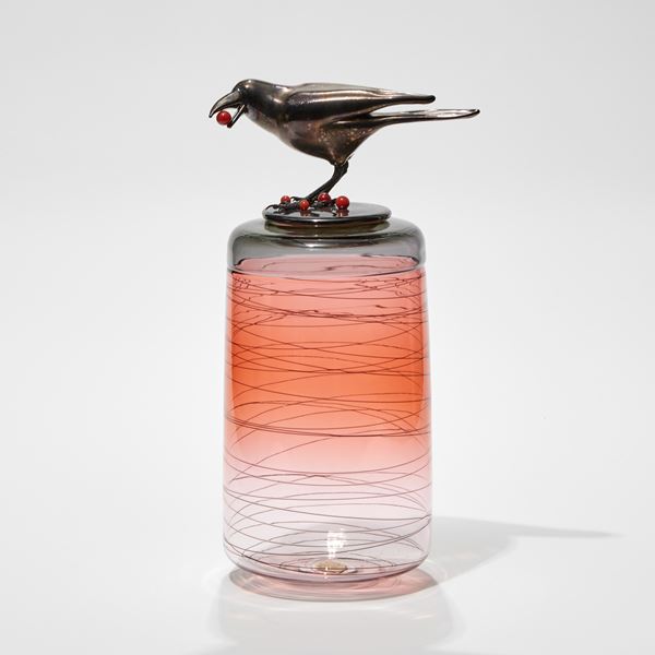 transparent apricot vase base with black lid with a crow perched on top with a cranberry in its mouth and berries at its feet hand made from glass