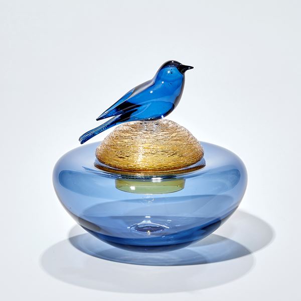 blue and golden amber low vase with smooth and textured surfaces and lid with a blue bird hand sculpted from glass