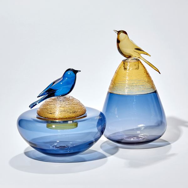 blue and yellow gold vessel with smooth transparent base with woven top detail and stopper adorned with a golden bird handblown from glass