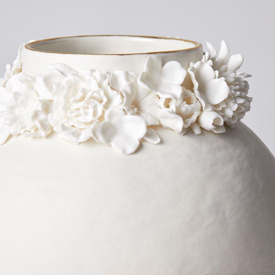 off white rounded vase with slightly rough texture and foot ring with flowers clustered round the neck opening with a final rim of gold lustre handmade from porcelain and parian