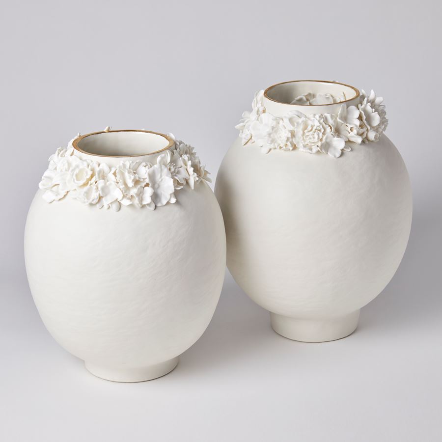 off white rounded vase with slightly rough texture and foot ring with flowers clustered round the neck opening with a final rim of gold lustre handmade from porcelain and parian