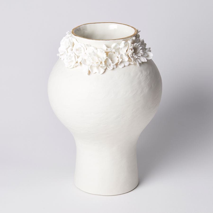 off white bulbous vase with narrow bottom half and slight rough texture with floral adornment around the neck which has a gold painted edge handmade from porcelain and parian