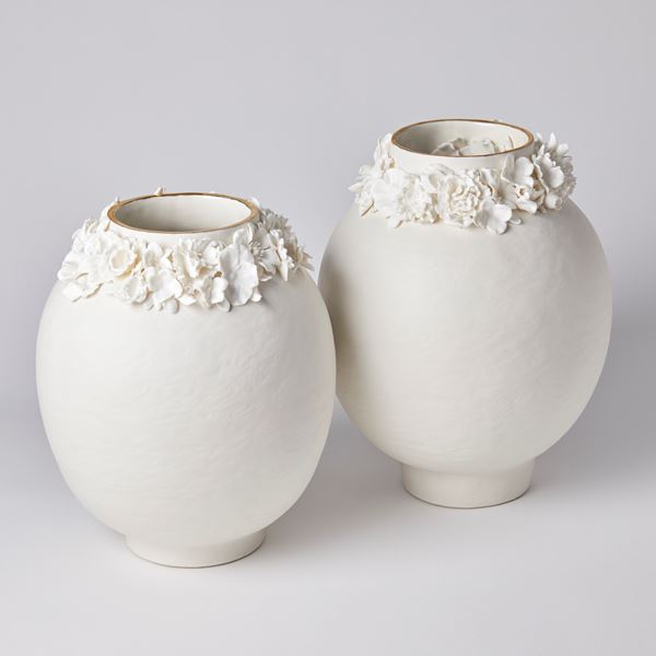 off white rounded vase with uneven surface and floral adornment around the opening with final band on gold on the rim handmade from porcelain