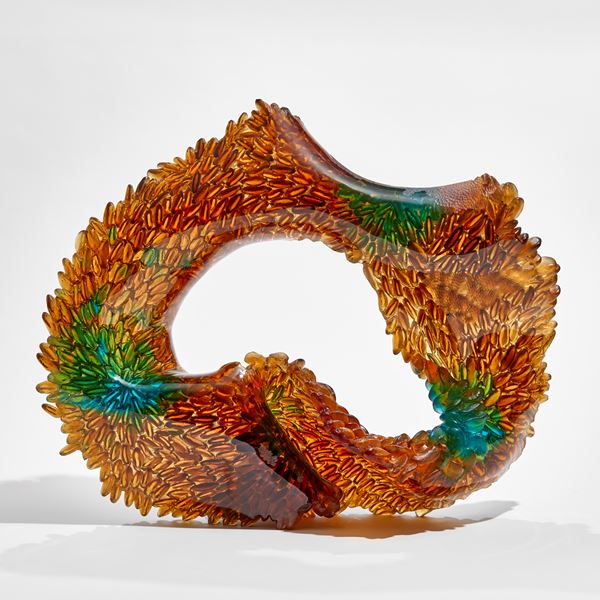 amber and green oval standing sculpture with one side with raised leaflike texture the other side smooth hand made from glass