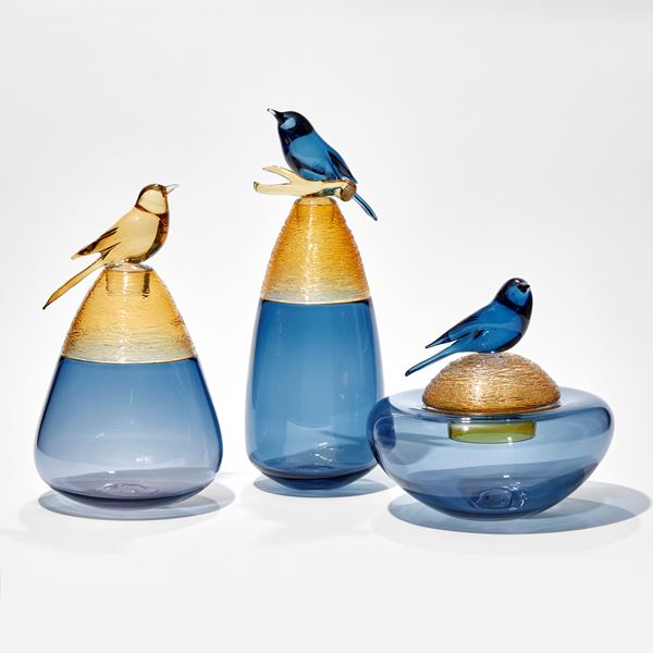blue teardrop shaped vase with the top third section in amber with woven spun texture and a stopper with a perched blue bird with yellow branch hand made from glass