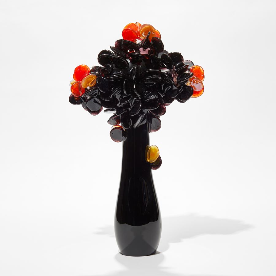 tall shiny black sleek simplified tree sculpture with top covered in clustered round lollipop leaves in black orange and amber hand made from glass