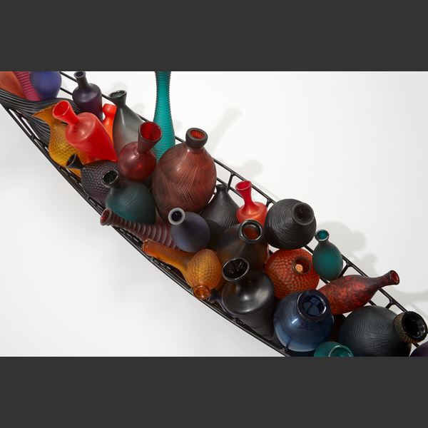 framework outlined simplified black boat hull filled with many single different coloured and shaped bottles hand made from glass