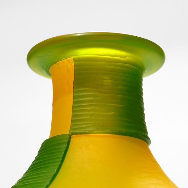 green and yellow amphora bottle with geometric square cut bold patterns on a black steel tripod stand handmade from glass