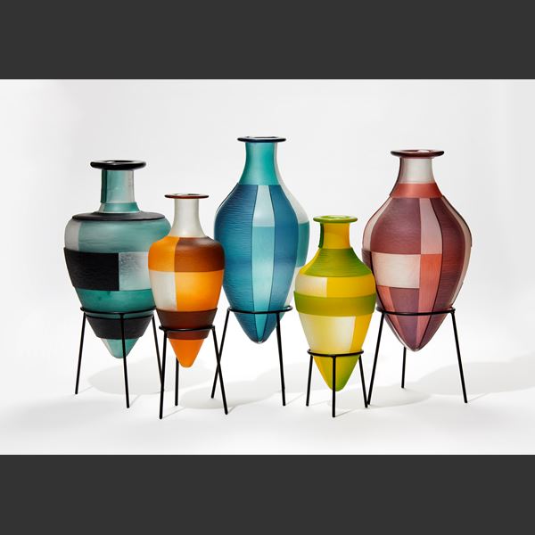 green and yellow amphora bottle with geometric square cut bold patterns on a black steel tripod stand handmade from glass