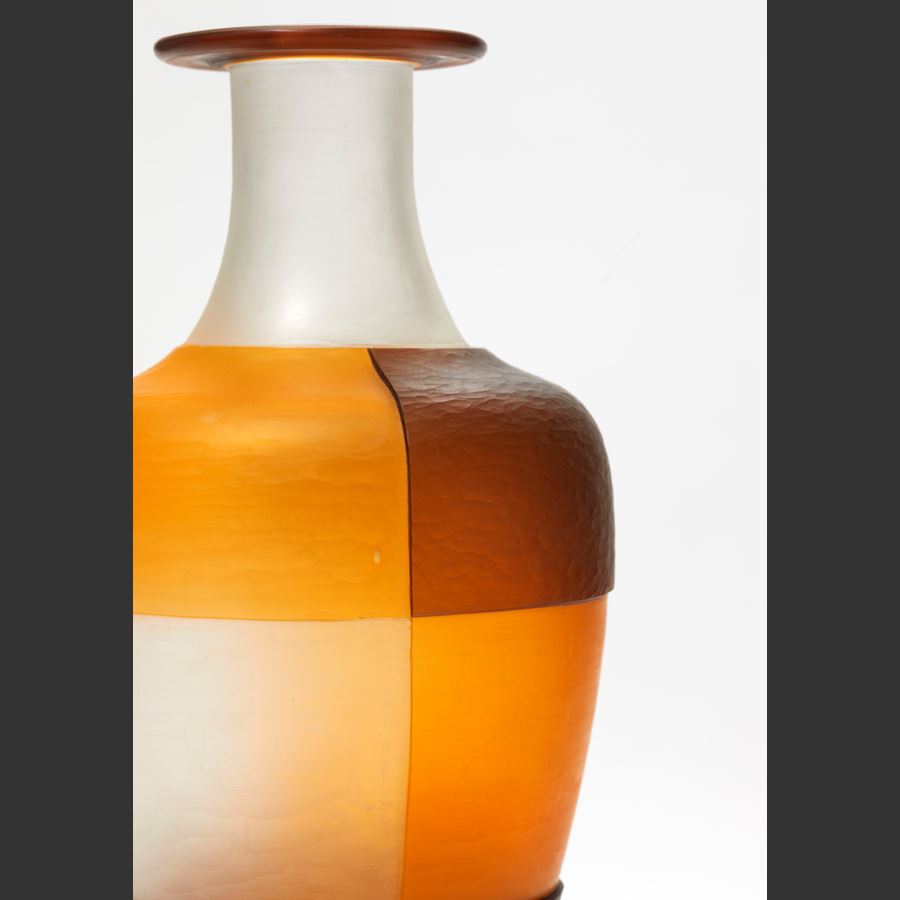 clean orange and brown bottle with block geometric square cut pattern perched on a black metal stand handmade from glass