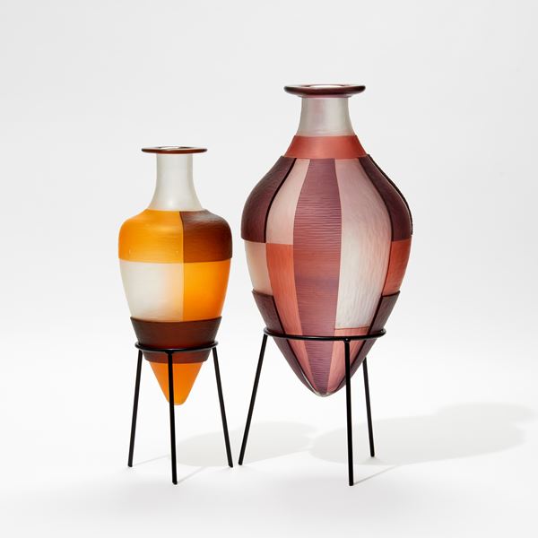 clean orange and brown bottle with block geometric square cut pattern perched on a black metal stand handmade from glass