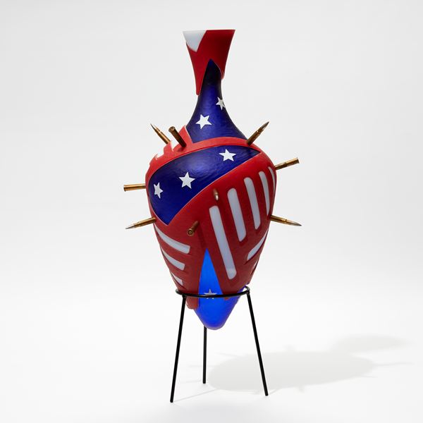 red white and blue amphora bottle with abstract stars and strips pattern pierced with bullets with a black metal stand